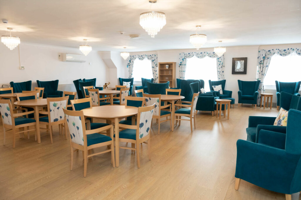 Dining area with laid wooden tables and chairs. The table clothes and chair backs and seats are blue/green colour.