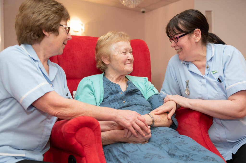 Elderly resident with two members of staff either side of them holding each of their hands.