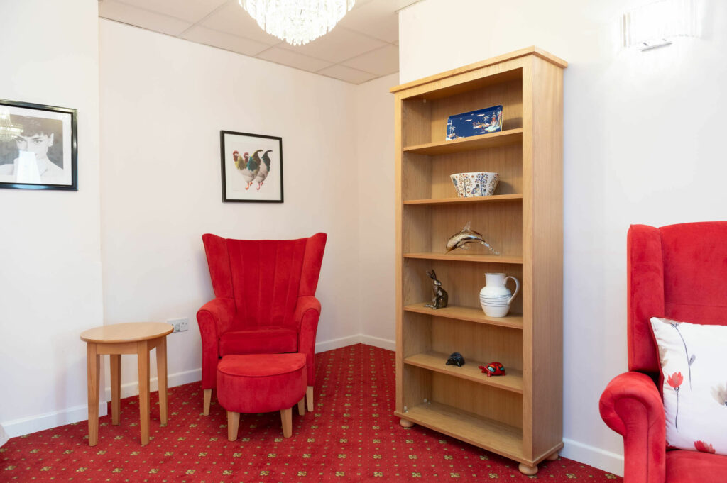 Red arm chair and footstool pictured beside a wooden stack of shelves.