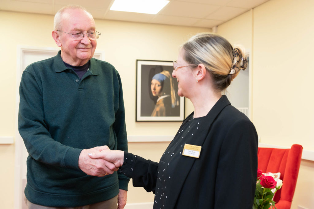 A member of staff shaking hands with an elderly resident.